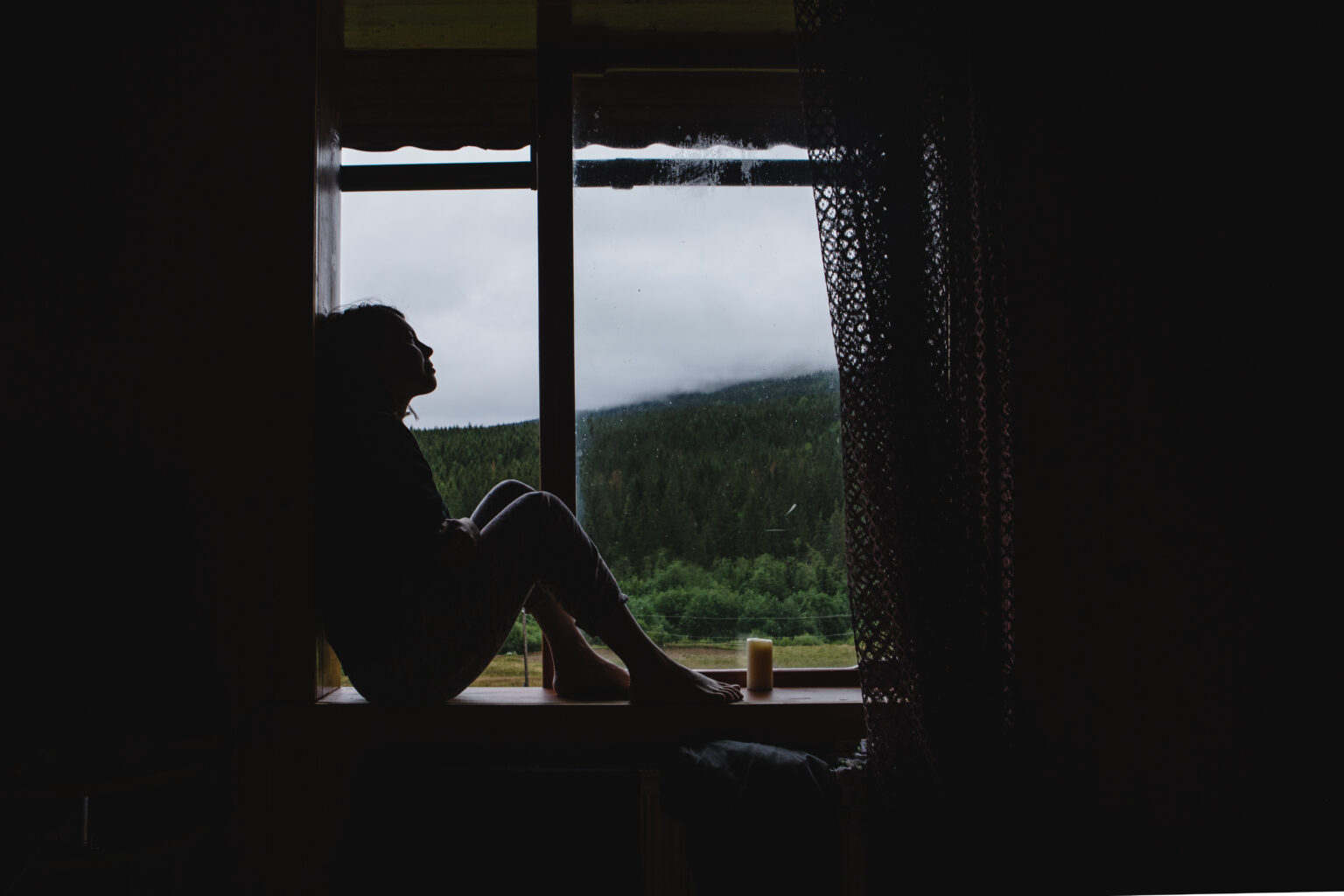 person sitting alone by a window processing survivor's guilt